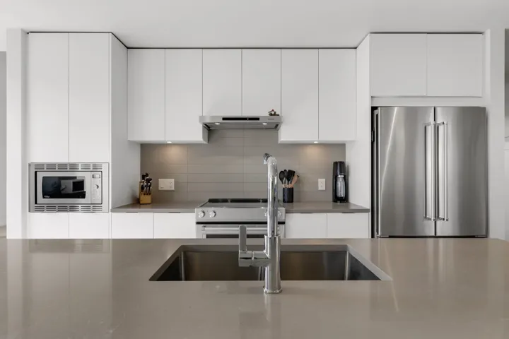 Kitchen featuring modern cabinets, stainless steel appliances, white cabinetry, and tasteful backsplash