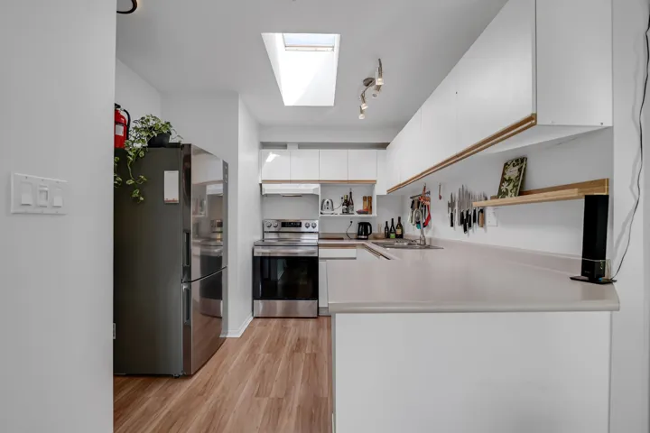Kitchen with a skylight, white cabinets, light wood-style flooring, stainless steel appliances, and open shelves