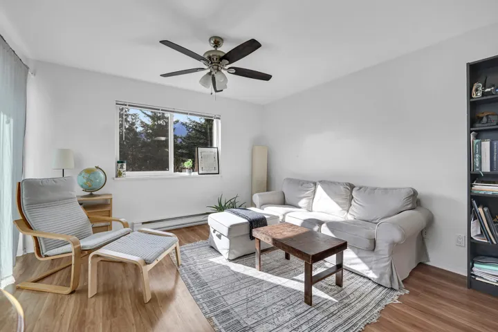Living room with ceiling fan, baseboard heating, and wood finished floors
