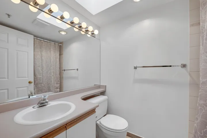 Full bath featuring a skylight, visible vents, toilet, curtained shower, and vanity