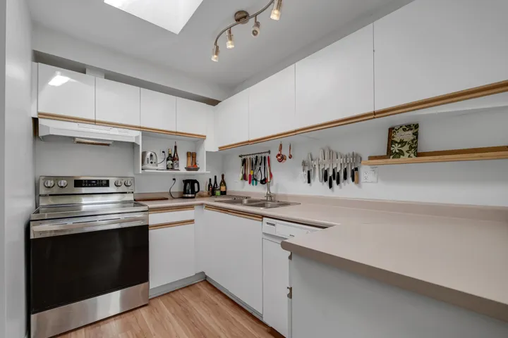 Kitchen with under cabinet range hood, a skylight, white cabinetry, stainless steel electric range, and light wood finished floors