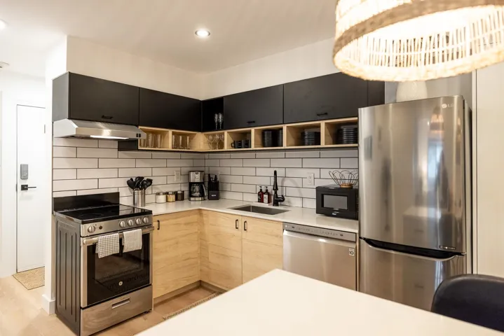 Kitchen featuring under cabinet range hood, open shelves, a sink, stainless steel appliances, and light countertops