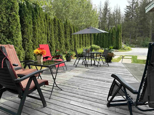 Expansive wood-finish deck with mature evergreen hedging, stone paver pathway, and surrounding natural landscaping