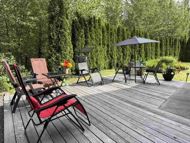 Wood-plank outdoor deck with concrete patio area, surrounded by lush green privacy trees and landscaping