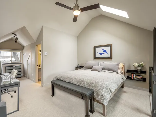 Bedroom featuring a ceiling fan, lofted ceiling with skylight, light carpet, and baseboards