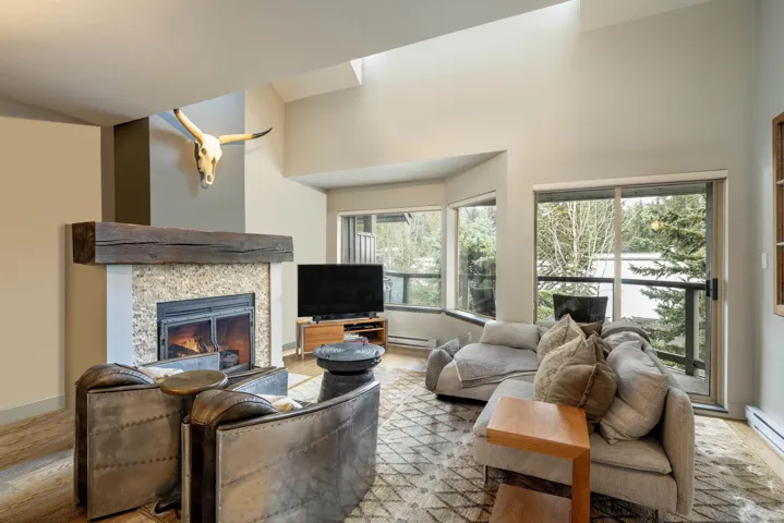 Living area with high vaulted ceiling, a tile fireplace, baseboards, baseboard heating, and light wood-style floors