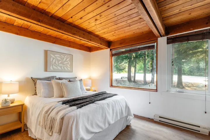 Wood-paneled ceiling with exposed beams, wood-finish flooring, and large windows with natural wood frames