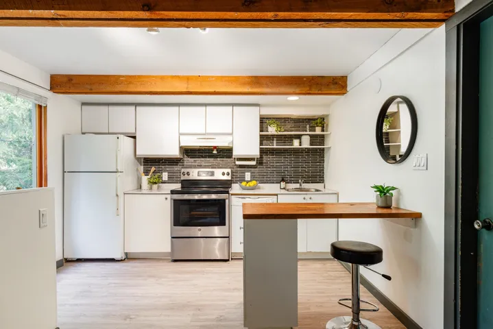 Kitchen featuring exposed wood beams, stainless steel range, white cabinetry, dark tile backsplash, and light wood-finish flooring