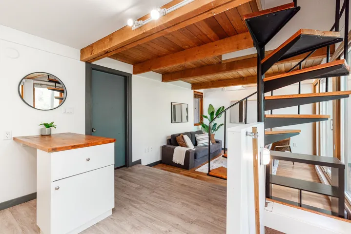 Exposed wood beam ceiling, spiral staircase with wood treads, wood-finish flooring, built-in white cabinetry with a wood countertop, track lighting