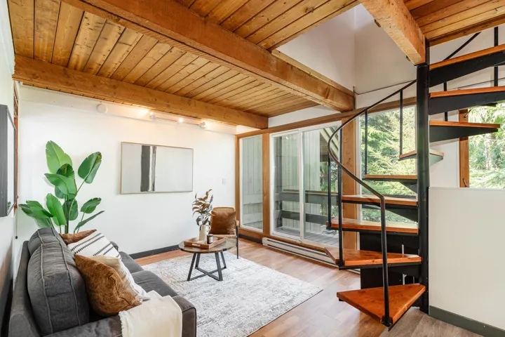 Wood-finish flooring with exposed wood beam ceiling, track lighting, sliding glass doors, and a spiral staircase with wood treads and metal railing