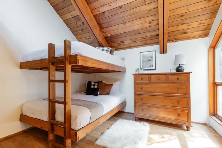 Vaulted wood plank ceiling with exposed beams, wood-finish flooring, built-in bunk beds, and a large window providing natural light