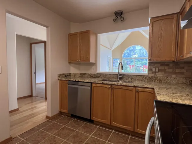 Kitchen featuring dishwasher, a sink, electric range oven, lofted ceiling, and exhaust hood