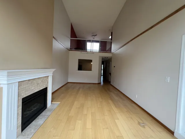Unfurnished living room featuring a brick fireplace, light wood-type flooring, baseboards, and a towering ceiling