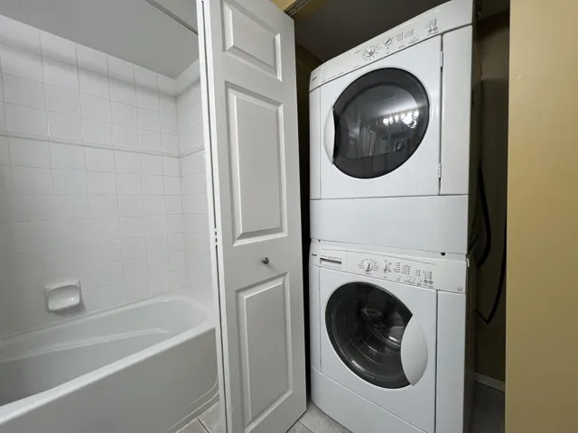 Washroom with stacked washer and clothes dryer and tile patterned flooring