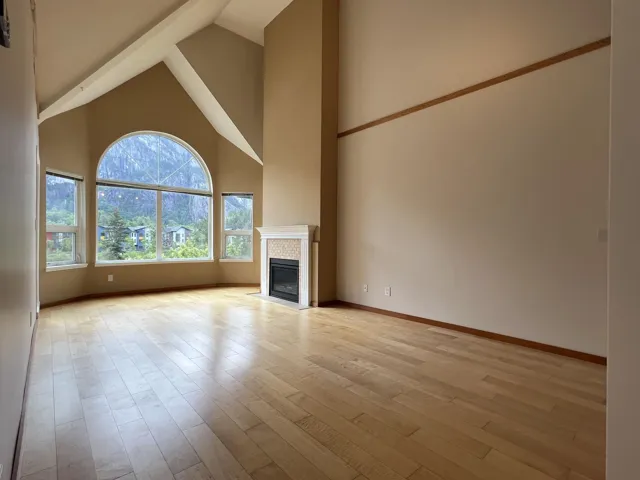 Unfurnished living room with high vaulted ceiling, light wood-style flooring, a tile fireplace, and baseboards