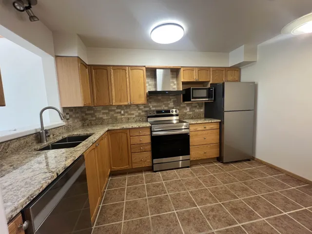 Kitchen featuring appliances with stainless steel finishes, wall chimney range hood, a sink, backsplash, and light stone counters