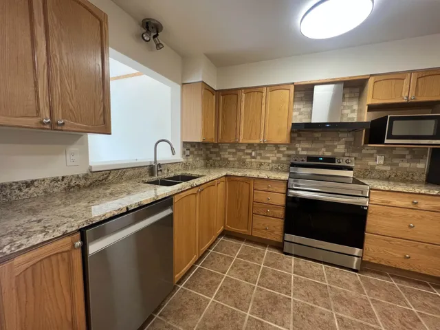 Kitchen with stainless steel appliances, a sink, wall chimney exhaust hood, and tasteful backsplash