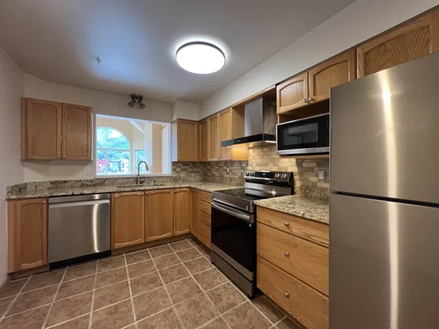 Kitchen with stainless steel appliances, wall chimney exhaust hood, a sink, backsplash, and light stone countertops