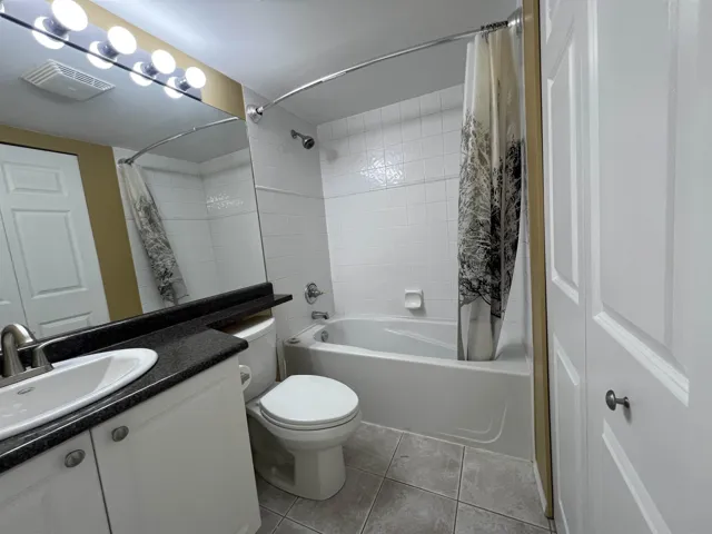 Full bath with shower / bathtub combination with curtain, vanity, tile patterned flooring, and toilet