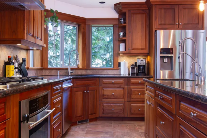 Kitchen with dark stone counters, decorative backsplash, brown cabinetry, appliances with stainless steel finishes, and under cabinet range hood