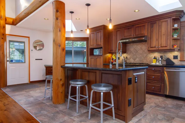 Kitchen featuring a skylight, open shelves, tasteful backsplash, dishwasher, and under cabinet range hood