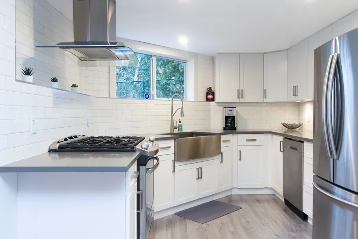 Kitchen with island exhaust hood, light wood finished floors, stainless steel appliances, backsplash, and white cabinets