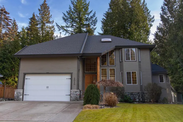 View of front of home featuring an attached garage, fence, driveway, stone siding, and a front lawn