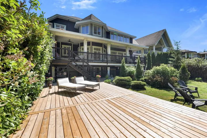 Expansive wood deck with a manicured lawn, established shrubbery, and mature trees