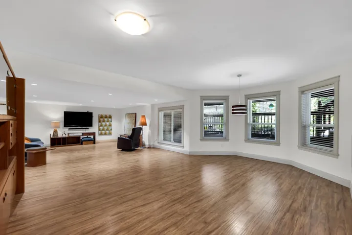 Spacious room featuring wood-finish flooring, recessed lighting, and multiple windows with grey trim