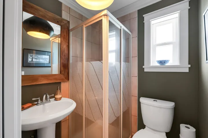 Compact bathroom featuring a glass-enclosed shower with frosted detailing, a pedestal sink with a chrome faucet, and a toilet