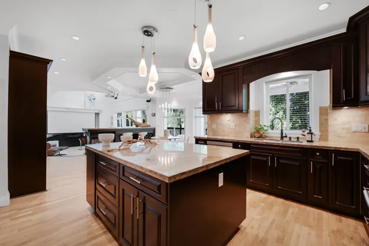 Open-concept kitchen featuring dark wood cabinetry, light wood-finish flooring, a central island with a light-toned countertop, recessed lighting, and pendant fixtures