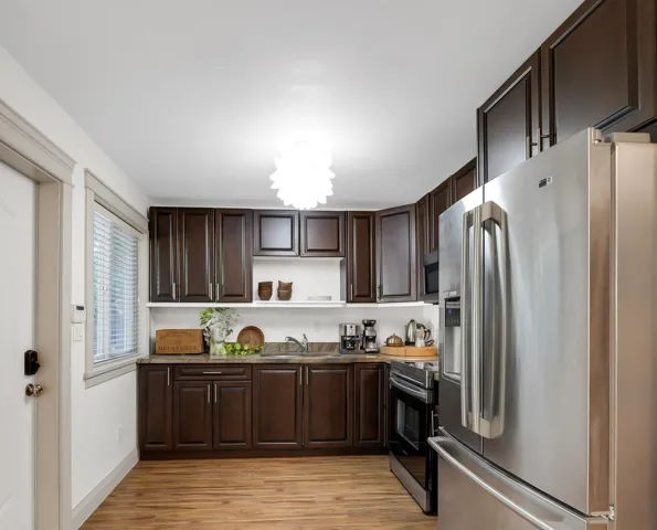 Kitchen featuring wood-finish flooring, dark wood cabinetry, stainless steel appliances, and a window with blinds