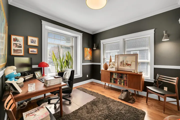 Room featuring dark wall paint with white crown molding and chair rail, wood-finish flooring, multiple windows with blinds, and built-in wall sconces