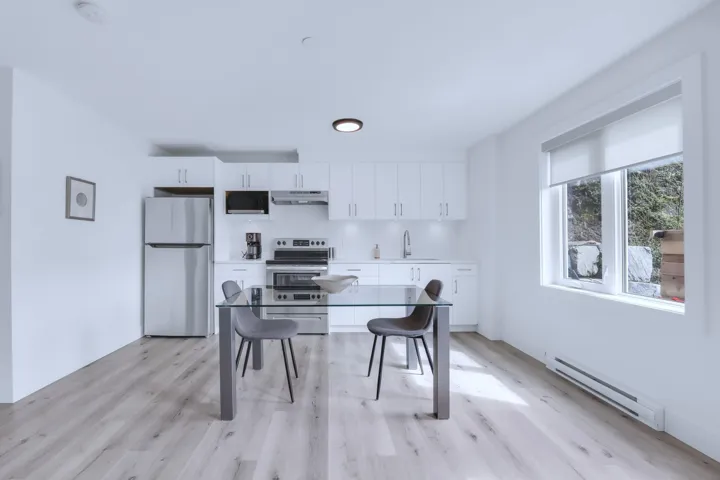 Kitchen featuring a baseboard heating unit, a sink, white cabinetry, under cabinet range hood, and appliances with stainless steel finishes