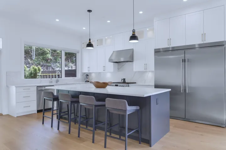 Kitchen featuring a kitchen breakfast bar, wall chimney exhaust hood, a center island, appliances with stainless steel finishes, and white cabinetry