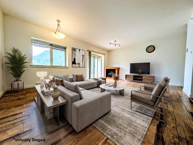 Virtually Staged - Spacious living area featuring wide-plank wood flooring, vaulted ceilings, and large windows