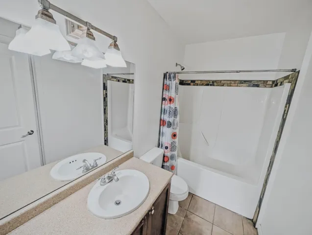 Bathroom featuring a vanity with two integrated sinks, an expansive mirror, and a bathtub with a tiled surround
