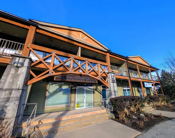 Multi-level commercial building featuring a wood and stucco exterior, prominent timber balcony railings, and multiple storefront entries