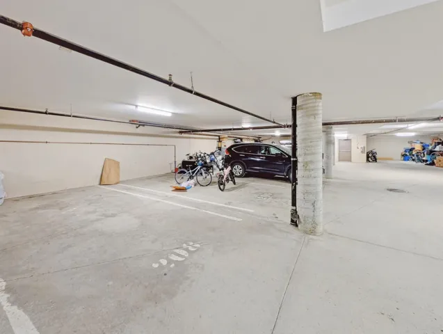 Concrete flooring in a subterranean parking area featuring overhead fluorescent lighting and exposed utility conduits