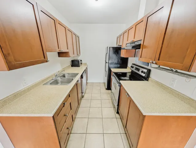 Galley kitchen featuring wood cabinetry, light-toned countertops, and tile flooring