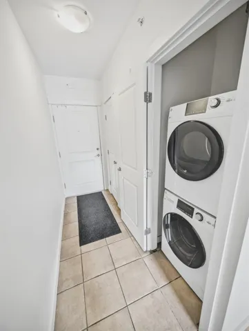 Entryway featuring tile flooring, white walls, and a recessed laundry area with a stacked washer and dryer unit