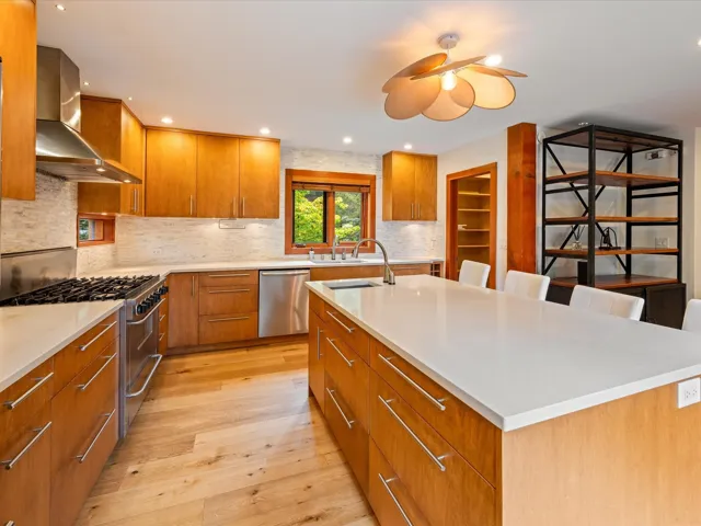 Modern kitchen featuring light wood-finish cabinetry, stainless steel appliances, a large center island with white countertops, light wood-finish flooring, and a decorative ceiling fixture