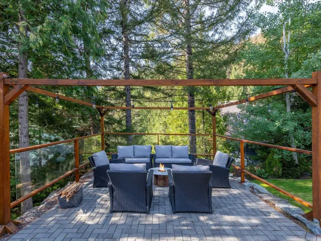 Paved patio area featuring a wooden pergola with string lighting and glass railings