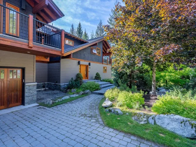 Multi-level residence featuring a natural wood-finish garage door, stone accents, and a prominent balcony with dark railings