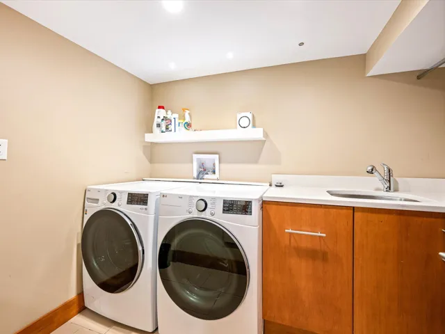 Dedicated laundry area featuring front-loading machines, a utility sink with a chrome faucet, and wood-finish cabinetry
