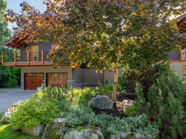 Exterior featuring two wood-finish garage doors, a stone block base, and a balcony with wood and metal railings