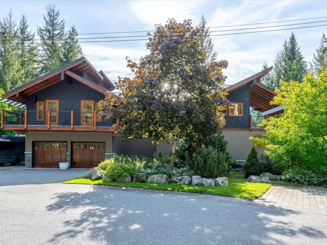 Contemporary architectural design featuring a two-car garage with wood-paneled doors, an elevated deck, and a distinctive roofline