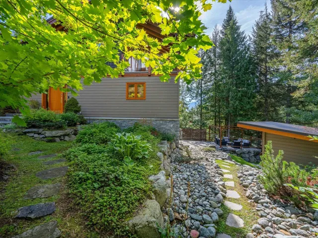 Exterior property showcasing a gray siding facade with wood-trimmed windows and door, stone foundation, and a lush, multi-level landscape