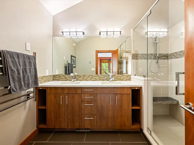 Bathroom featuring a dual-sink vanity with wood-finish cabinetry, a large frameless mirror, and overhead contemporary lighting