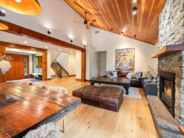 Spacious living area featuring a vaulted wood-paneled ceiling, stone fireplace with a wood mantle, exposed wood beams, and light wood-finish flooring